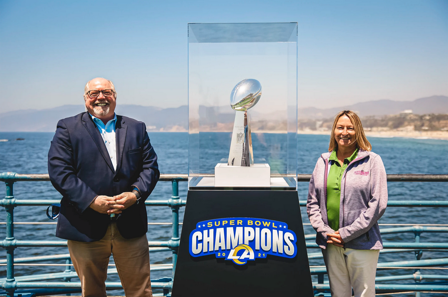 Rams fans stand next to the Vince Lombardi Super Bowl Trophy with views of Santa Monica Beach in the background.